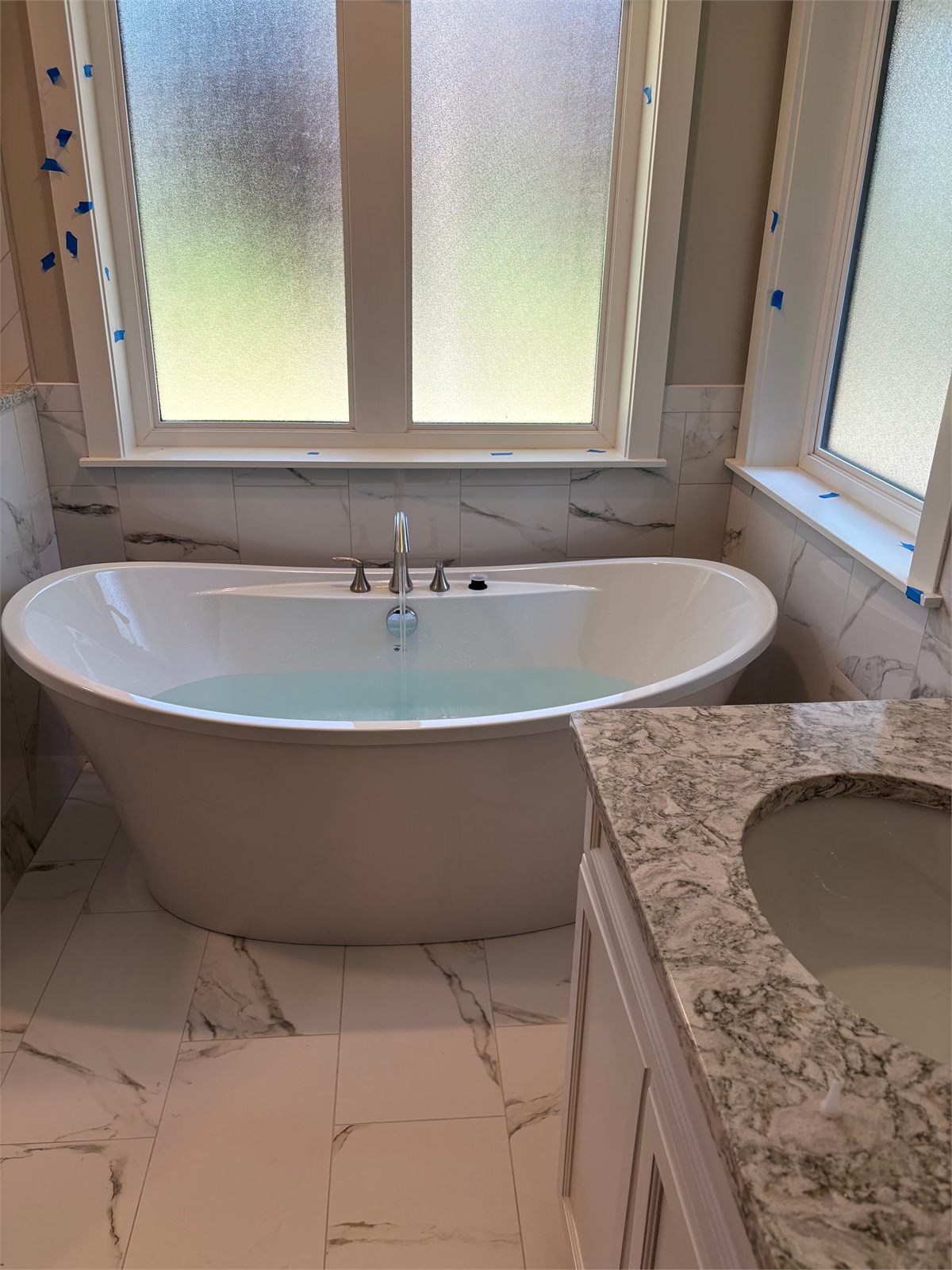 Freestanding soaker tub installed against full-height marble tile in a new master bathroom